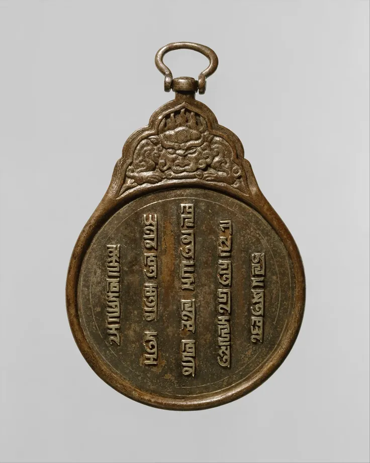 Fotografia de uma placa de ferro escurecido em forma de pera, com uma argola no alto; o topo traz em relevo a cabeça de uma fera de juba, e o disco é coberto por cinco colunas verticais de caracteres em escrita phags-pa, incrustados em prata.